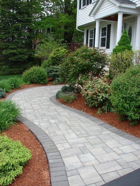 Curvilinear landscape curbing made of interlocking concrete pavers, flanked by shrubs and red mulch for contrast and moisture retention.