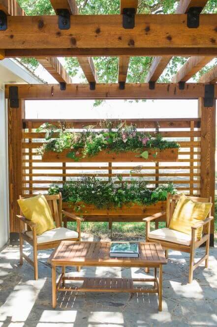 Cozy seating under a wooden pergola with soft cushions, a low coffee table, and a vertical garden backdrop, ideal for budget-friendly landscaping.