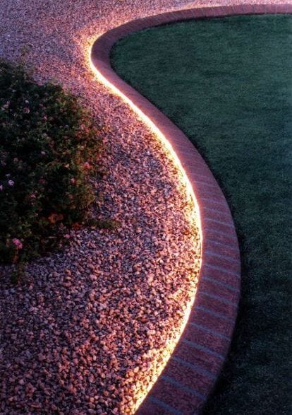 Elegant curved gravel edging with low-voltage LED lights, transitioning to a lush lawn, enhances safety and ambiance in landscape curbing design.