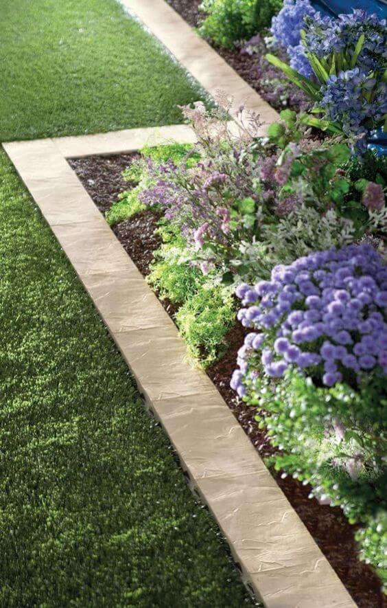 Artificial turf surrounded by 4-inch concrete curbing frames a vibrant flower bed, enhancing the transition between hard and soft landscaping.