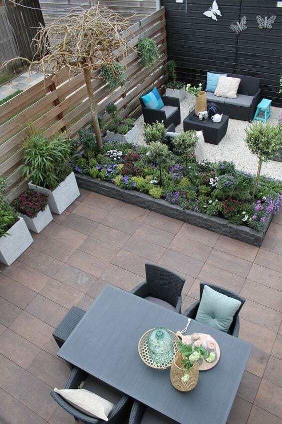Compact modern garden design featuring dark wooden slats and vibrant flower beds. A stylish patio with contemporary furniture enhances the inviting space.