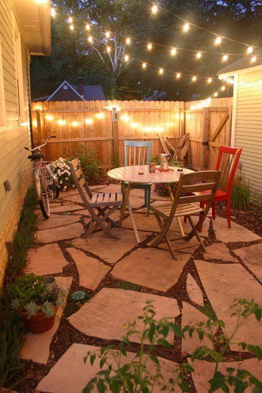 Quaint patio with natural stone flooring, colorful metal chairs, and string lights, ideal for budget-friendly backyard gatherings.