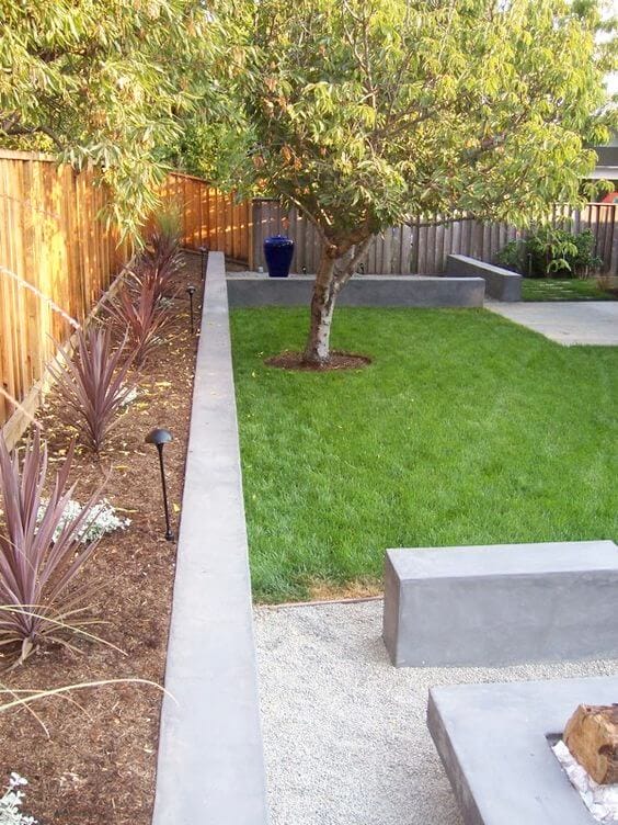 Thoughtfully designed landscape with a green lawn bordered by low concrete curbing, accent plants, and a gravel seating area.
