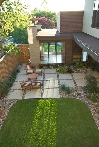 Patio area with large concrete slabs and gravel, featuring wooden chairs around a circular table. Surrounded by native shrubs, it offers a low-maintenance, modern aesthetic.