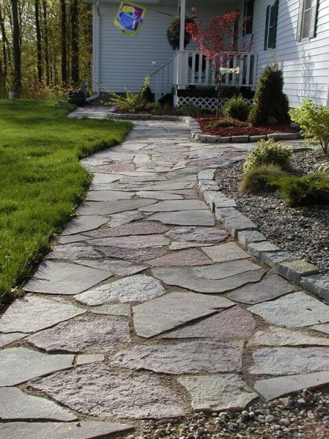 Curved stone pathway made of flagstone, bordered by a manicured lawn and decorative plants, enhancing the landscape curbing design.