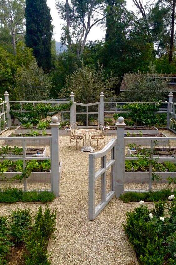 Meticulously designed garden with four raised beds, a central seating area, and trimmed shrubs, all enclosed by a wooden fence.