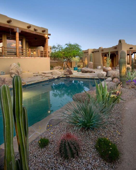 Serene pool area with desert landscaping, featuring native plants like tall cacti and succulents, bordered by gravel and boulders.