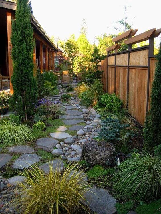 Thoughtfully designed pathway of irregular flagstone stones, bordered by diverse plantings, leading through a lush garden with a wooden fence.
