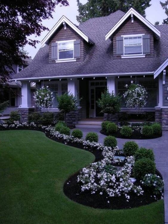 Structured front yard design featuring manicured lawn, trimmed shrubs, and blooming white flowers in curved beds, enhanced by dark mulch.