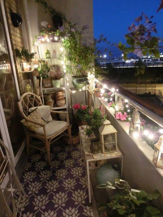 Cozy balcony with a rattan chair and cushion, lush potted plants, string lights, and vibrant flowers, creating a charming outdoor retreat.