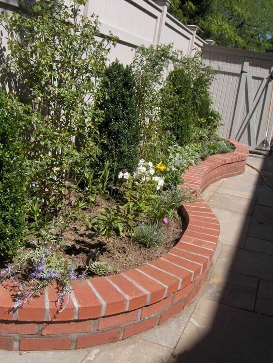 Curved brick planter bed defining a garden area, featuring red brick construction, flowering perennials, and shrubs for seasonal interest.