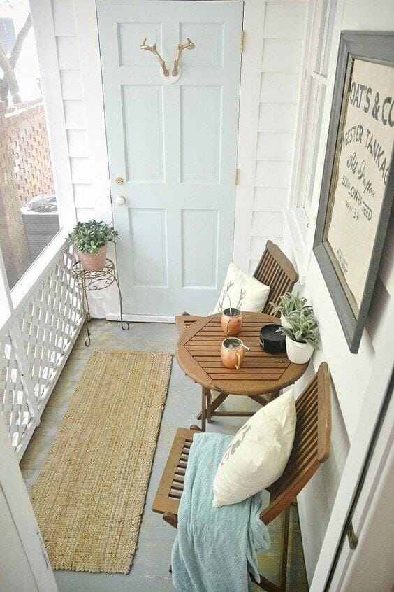 Compact terrace design featuring a light blue door, wooden folding chairs, and a round table, enhanced by potted plants and a jute runner.