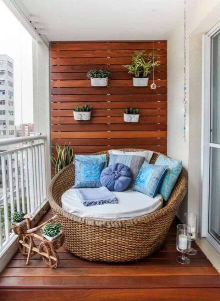 Circular rattan lounge chair on a wooden deck, surrounded by a vertical slat wall and five colorful potted plants, perfect for small terrace design.