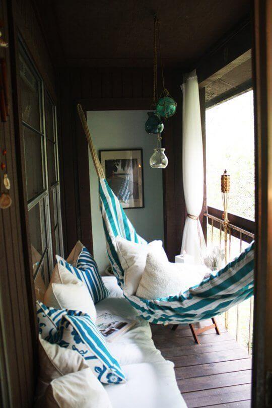 Inviting hammock space on a wooden deck features striped cushions, light furnishings, and decorative elements, ideal for small outdoor retreats.