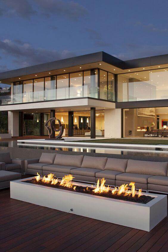 Outdoor fire feature with built-in flames, surrounded by modern sectional sofa on a dark wood deck, creating a cozy social space.