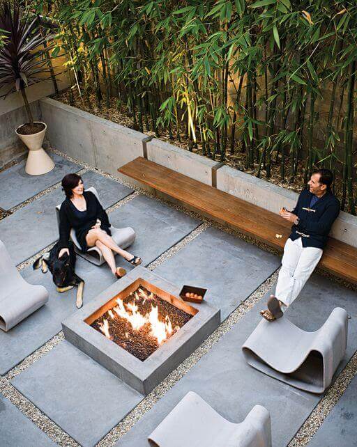 Central fire pit surrounded by hexagonal concrete pavers, with molded fiberglass benches and bamboo privacy screen, creating a modern, cozy backyard.