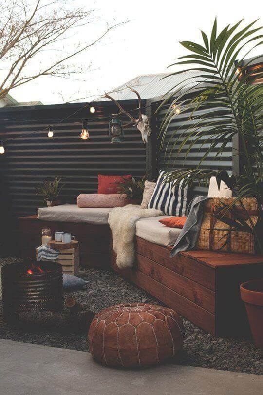 Cozy outdoor lounge area with a wooden platform, soft cushioned seating, ambient lighting, and potted plants, ideal for relaxation.