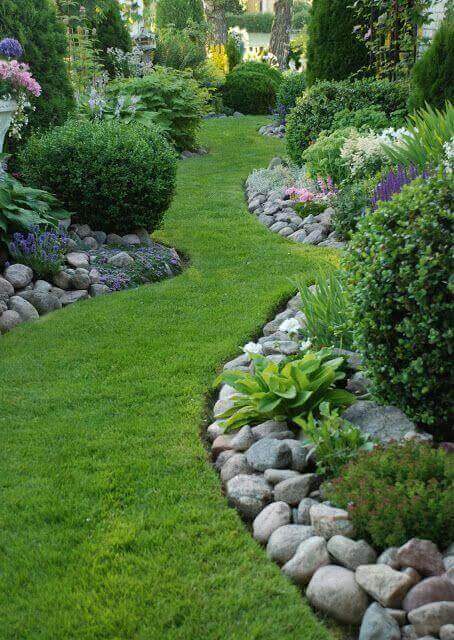 Winding pathway bordered by smooth river stones and lush grass, flanked by manicured hedges and vibrant flower beds, showcasing DIY garden design.