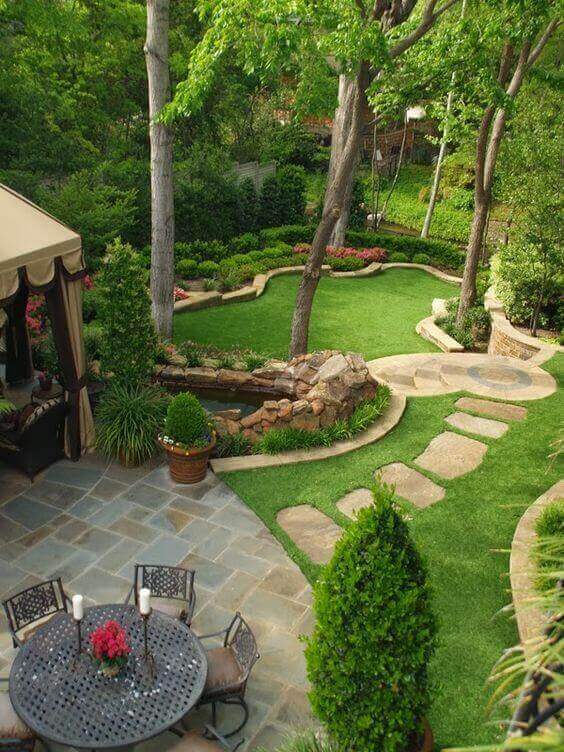 Landscaped garden with stone pathways, flower beds, and ornamental trees, featuring a round metal dining table and climate-appropriate plants.