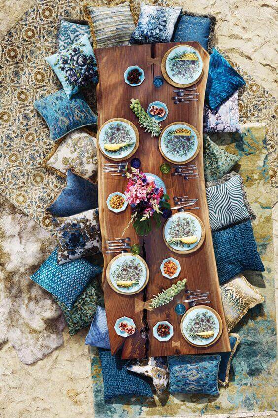 Outdoor dining setup with a long live edge walnut table, adorned with plates and cushions, reflecting a bohemian style.