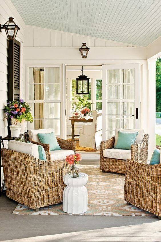 Spacious back porch with woven wicker chairs, a small coffee table, light blue ceiling, and white walls. Lanterns provide cozy evening lighting.