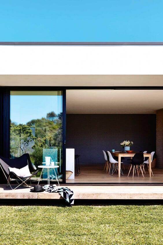 Modern patio showcasing sliding glass doors connecting to an open living area, featuring a light wood dining table and black chairs.