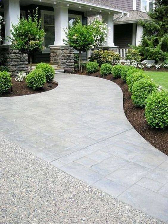 Curving concrete walkway with a textured finish, bordered by low-maintenance boxwood shrubs and dark mulch, enhancing front yard curb appeal.