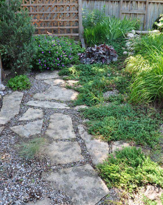 Natural stone pavers form a 24-inch wide flagstone walkway, bordered by gravel and lush ground cover plants, enhancing accessibility.