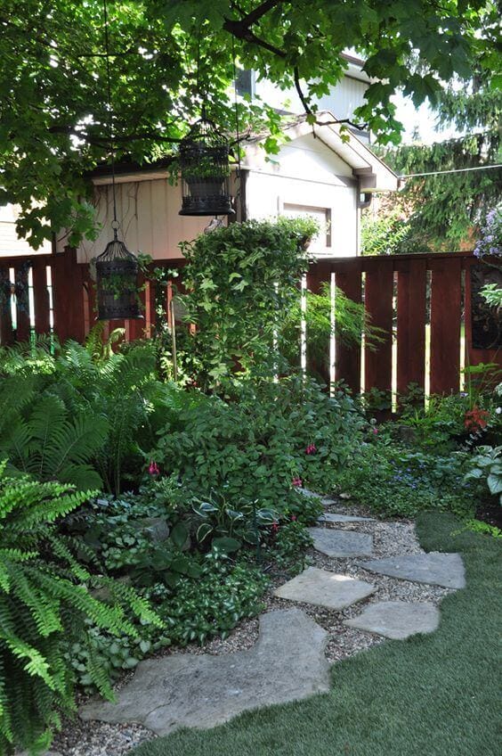 Flagstone and gravel walkway in a lush garden, bordered by ferns and flowering shrubs, leading through a serene environment.