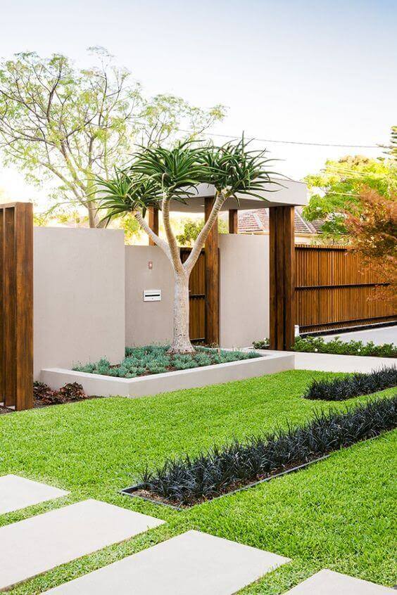 Frontyard landscape features undulating grass, a mature tree in a concrete planter, and stone paver pathways for enhanced curb appeal.