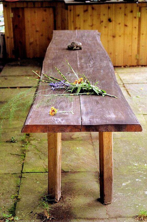 Long live edge dining table made of solid walnut, measuring 2.5m x 0.8m, adorned with flowers in a semi-shaded outdoor setting.