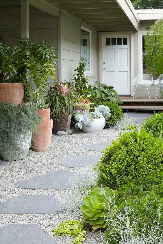 Flagstone and gravel walkway leads to a modern entryway, surrounded by potted plants and manicured boxwood shrubs for a vibrant landscape.