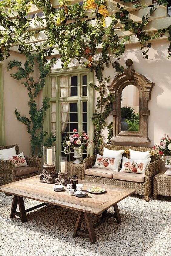 Cozy outdoor seating with two woven rattan sofas, rustic wooden table, and climbing greenery from a pergola, ideal for relaxation.