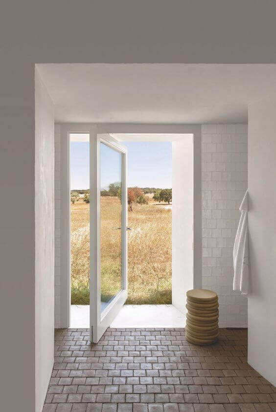 Patio doors open to a bright interior with white tiles, leading to golden fields through double glass doors, enhancing natural light.