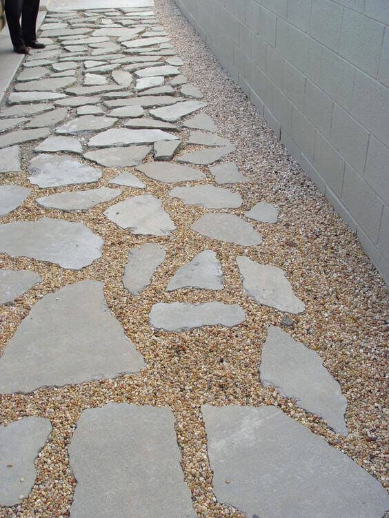 Flagstone and gravel walkway features irregular stone slabs in a 2-foot wide pathway, bordered by a concrete wall, enhancing accessibility.