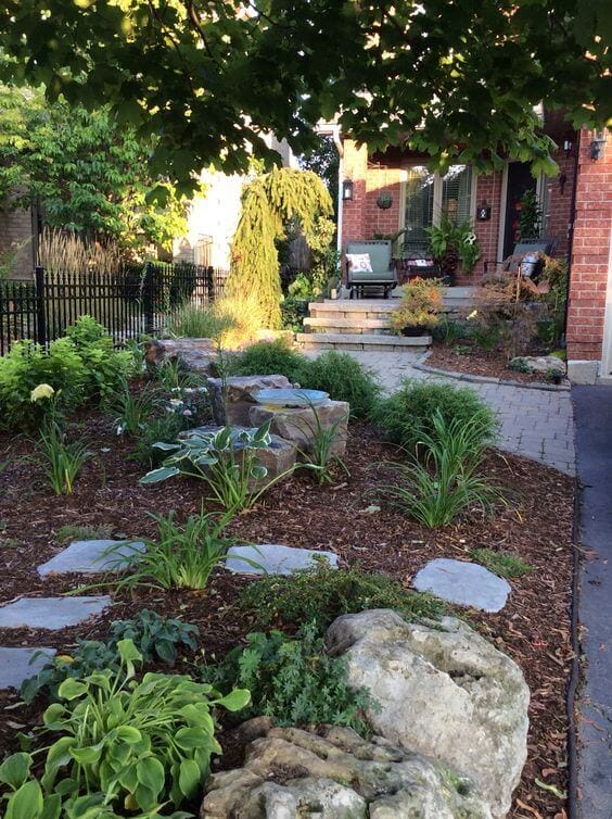 Thoughtfully designed front yard landscape featuring stone pathways, lush greenery, ornamental grasses, and a wrought-iron fence.