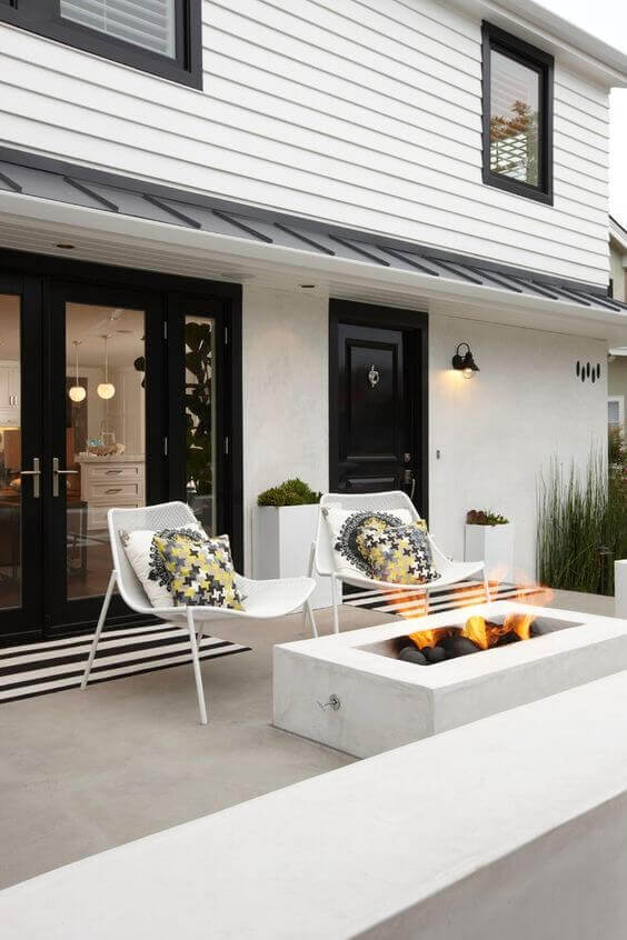 Modern patio layout featuring minimalist design, two white lounge chairs, and black-framed sliding doors contrasting with a white house exterior.