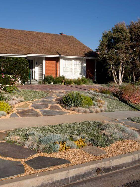 Flagstone and gravel walkway leading to a house entrance, framed by drought-resistant plants in earth tones and greens.
