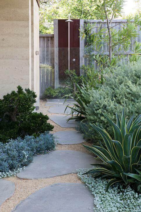 Pathway design features flagstone slabs in a meandering layout, bordered by drought-tolerant plants, leading to an outdoor shower.