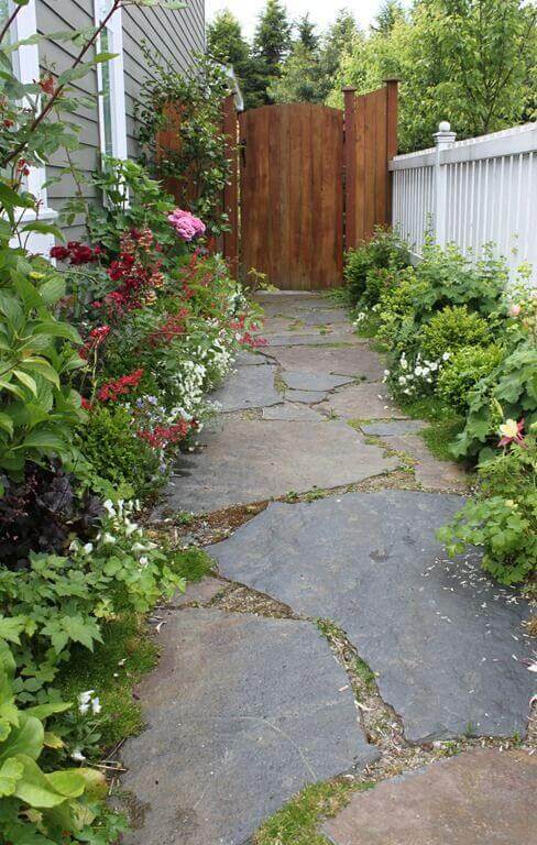 Natural stone pathway made of irregular slate slabs, bordered by lush plantings and a stained cedar gate, enhancing the rustic ambiance.