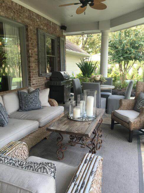 Cozy outdoor living space with a covered patio, featuring wicker furniture, a reclaimed wood coffee table, and potted plants.