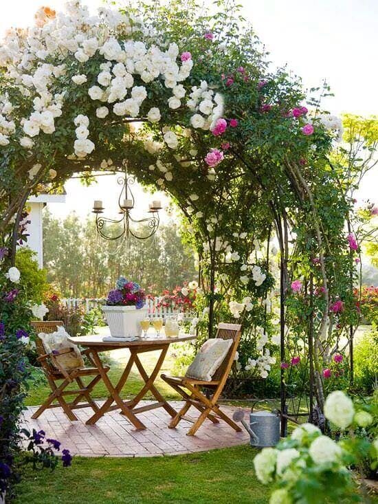 Charming outdoor seating framed by climbing roses, featuring a wooden table and chairs on a brick-patterned patio, ideal for relaxation.