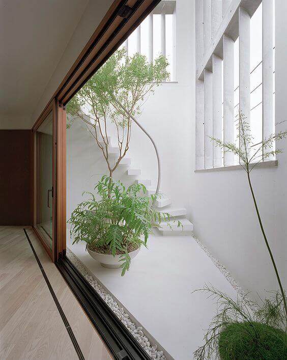 Patio door ideas showcase a minimalist space with a spiral staircase, natural light, and greenery in modern ceramic pots on gravel.