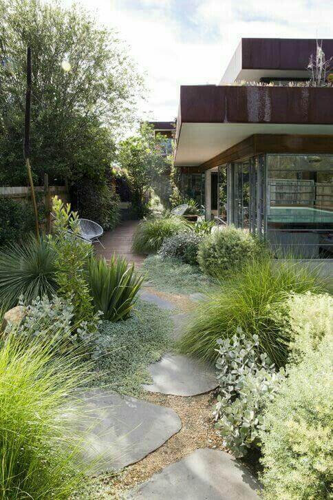 Flagstone and gravel walkway meanders through a lush garden, featuring ornamental grasses and low-growing ground cover plants.