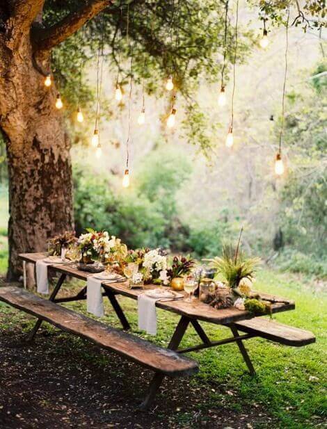 Long rustic live edge dining table beneath a large tree, adorned with floral centerpieces and candles, creating a warm, inviting outdoor atmosphere.