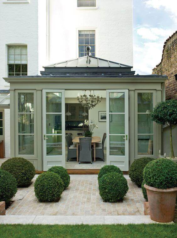 Contemporary conservatory with large glass doors and peaked roof, surrounded by boxwood hedges and York stone pavers for easy access.