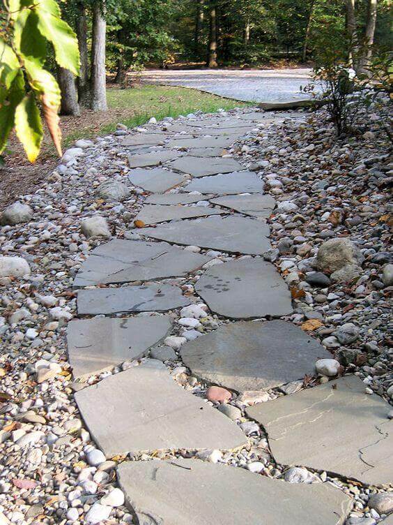 Irregularly shaped flagstone slabs set on river rocks form a naturalistic walkway winding through a shaded wooded area.