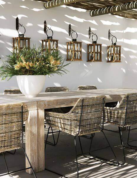Rustic live edge dining table, 240 cm long, surrounded by six woven chairs. Decorated with lanterns and a lush plant centerpiece.