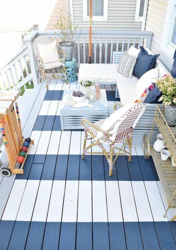 Cozy back porch featuring a checkerboard deck of blue and white planks, a sectional sofa, potted plants, and a reclaimed wood coffee table.