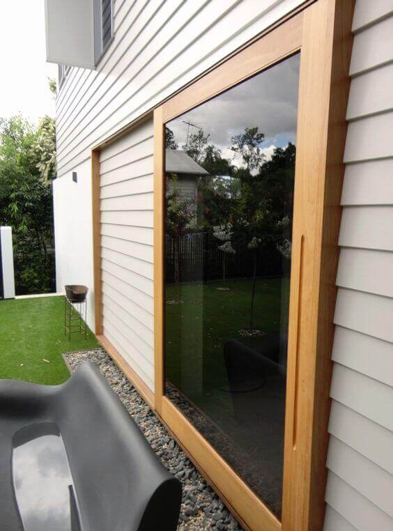 Post-modern patio design with large glass panels, a sleek black lounge chair, and a landscaped area featuring artificial grass and pebbles.